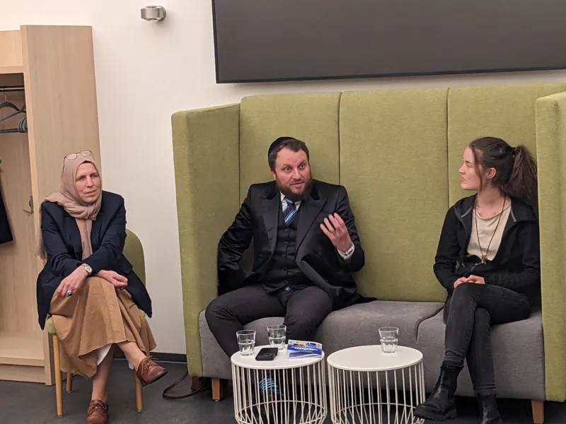 A rabbi in open conversation with two women on a sofa